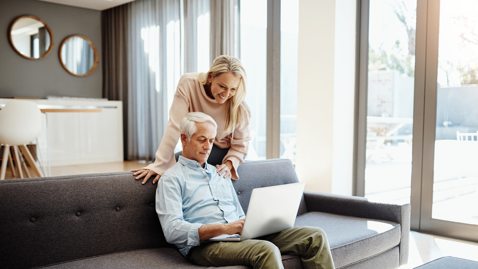 Oudere man op bank met laptop met vrouw die over schouder meekijkt
